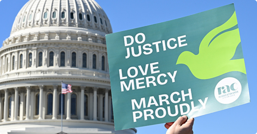 In front of the capitol building in Washington, DC, a person holds a RAC sign that reads: "Do Justice, Love Mercy, March Proudly." 